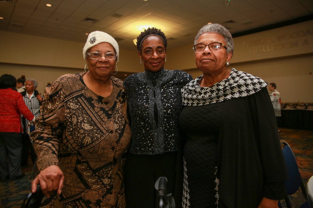 Three women pose for the camera in a large ballroom.
