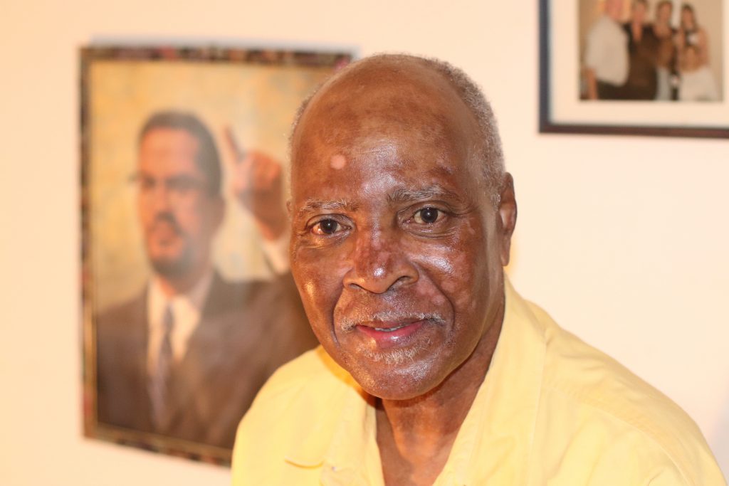 Closeup headshot of a man in a yellow shirt smiling at the camera.