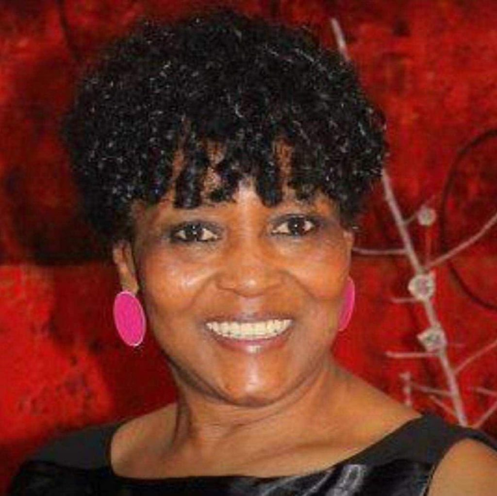 A closeup headshot of a woman smiling in front of a red backdrop.
