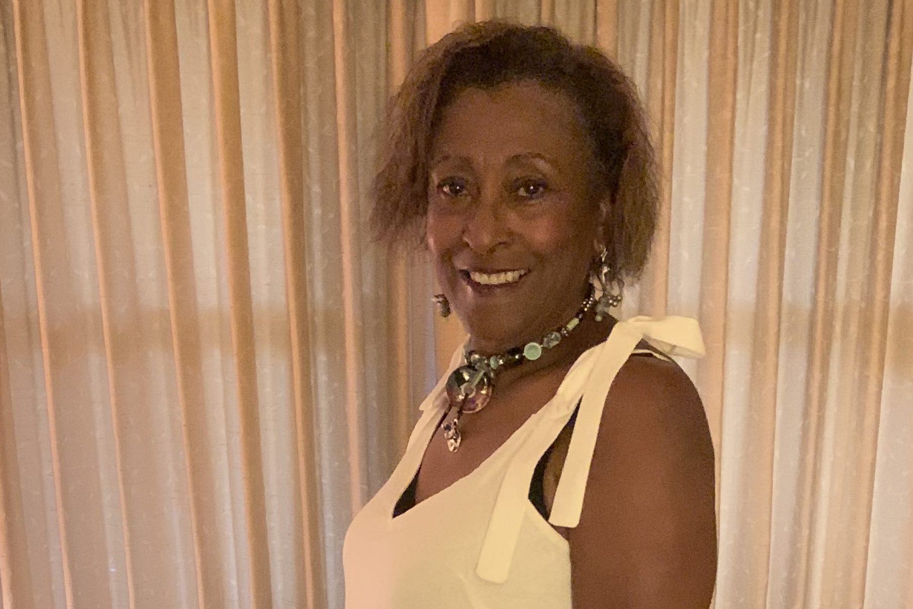 A woman in a dress poses for the camera in front of a couch in a house.